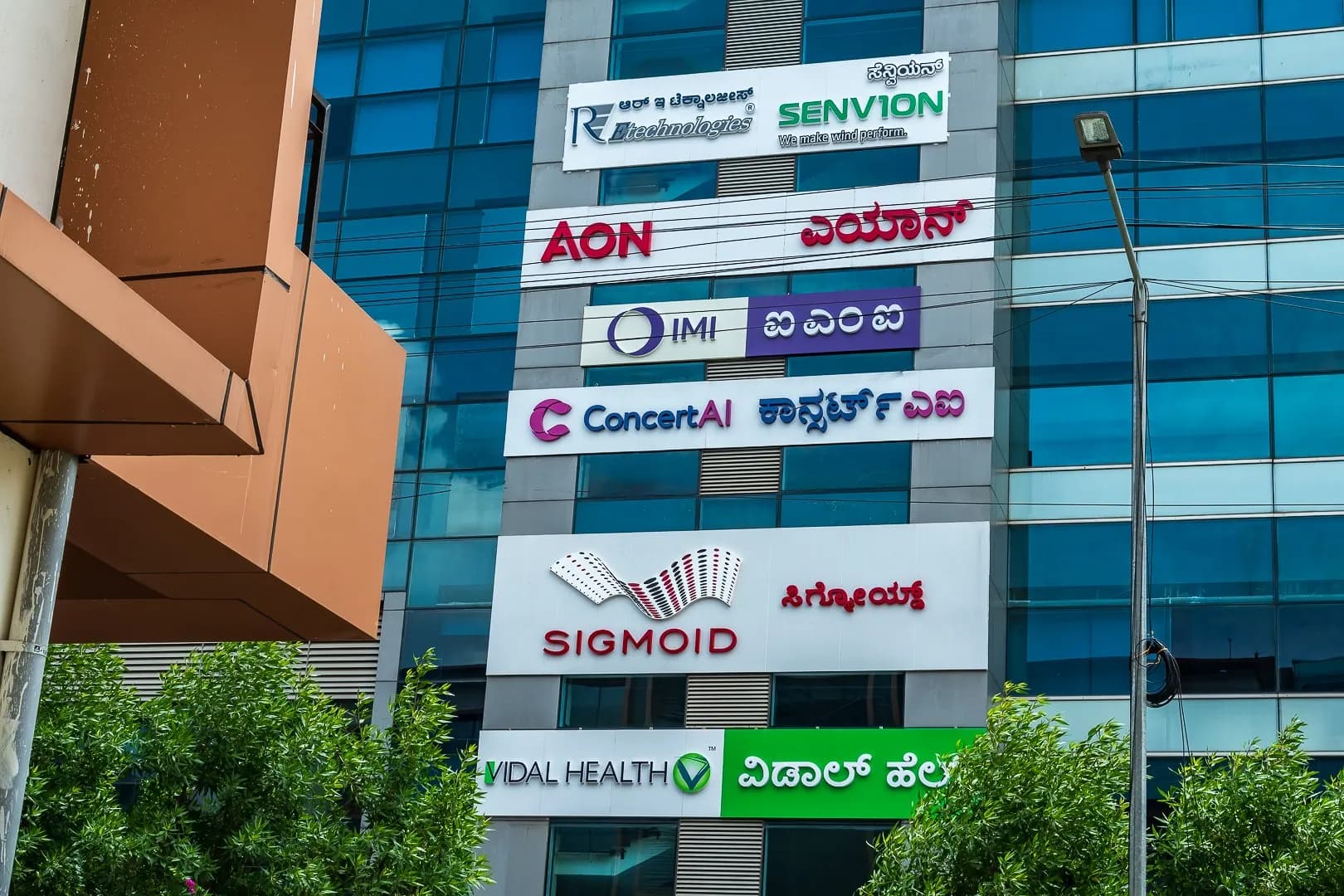 Stack of tenant signs on a glass tower, including Aon, ConcertAI, Sigmoid and Vidal Health