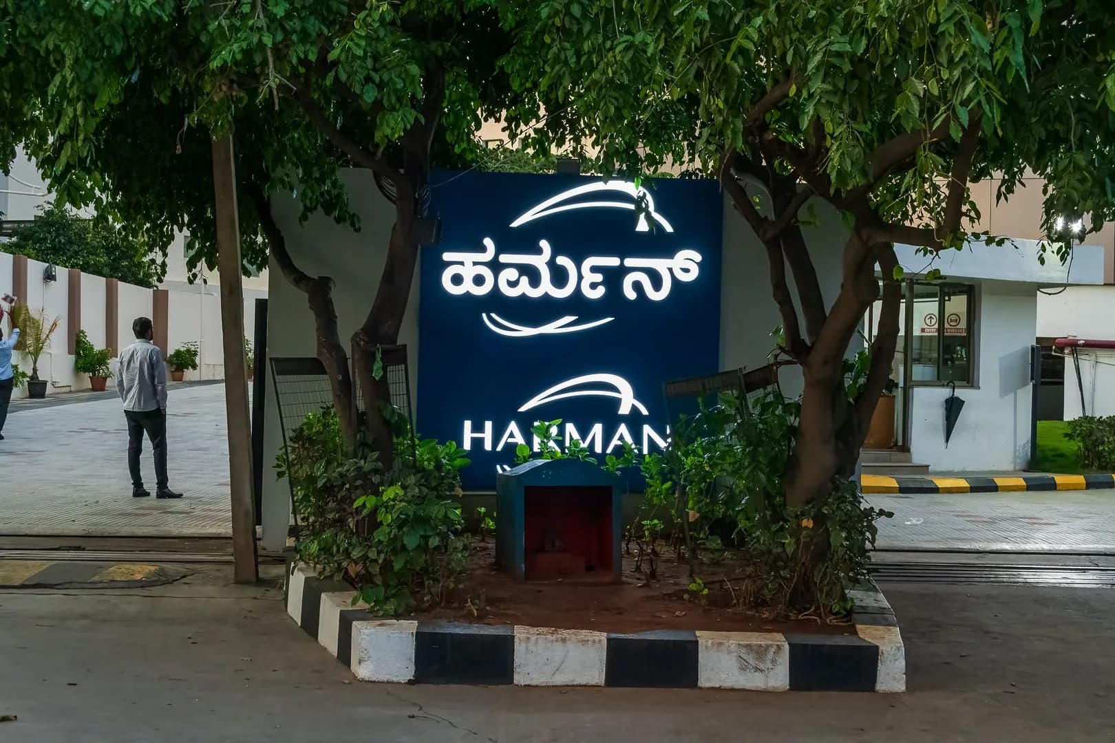 Harman entrance sign in Kannada and English under trees at the campus gate