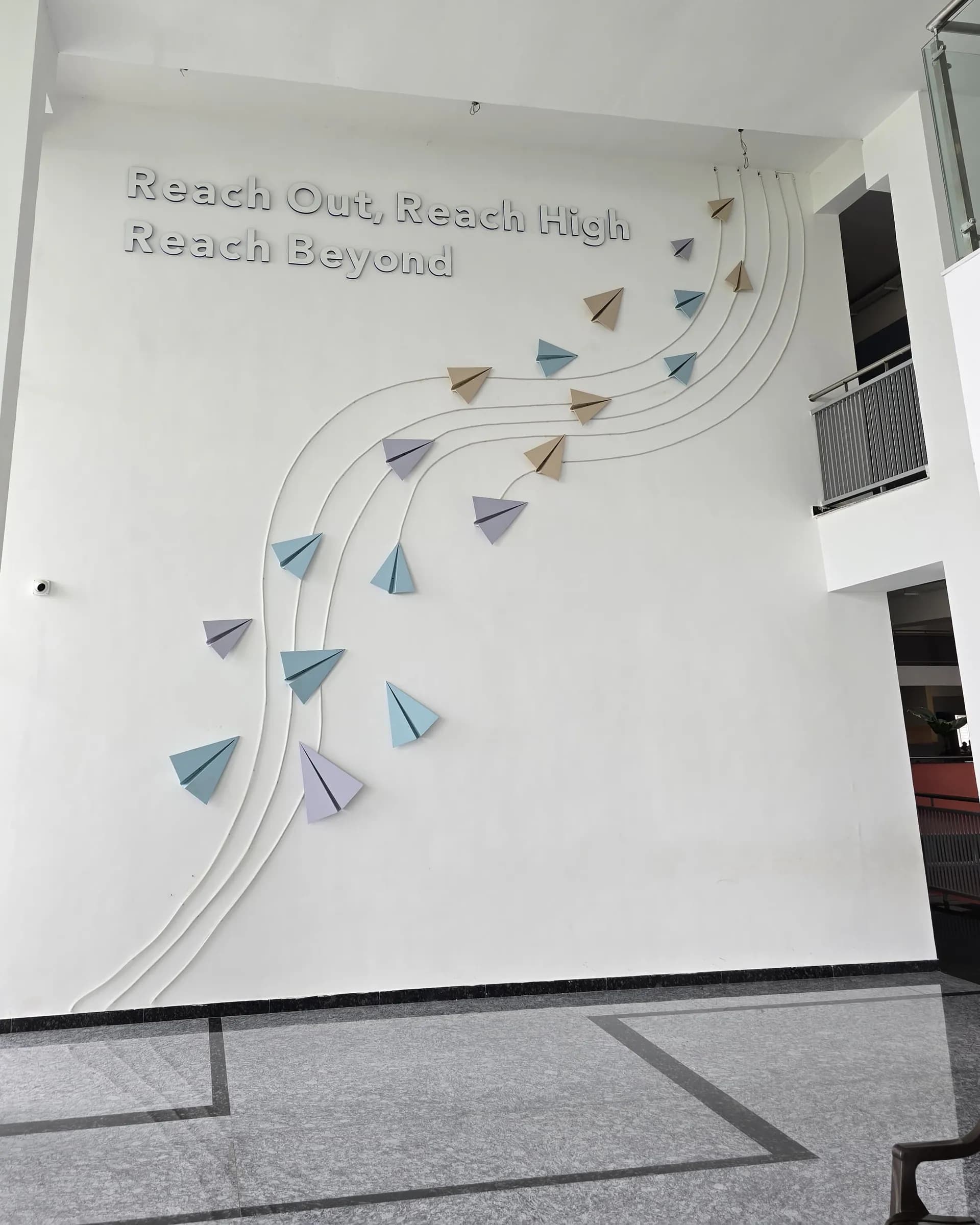 Double-height white wall with Reach Out, Reach High, Reach Beyond in raised letters and dimensional paper planes following raised flight paths