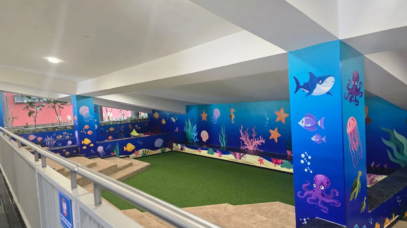 Under-stair play area with a pillar wrapped in a shark, octopus and jellyfish graphic, ocean walls and green turf