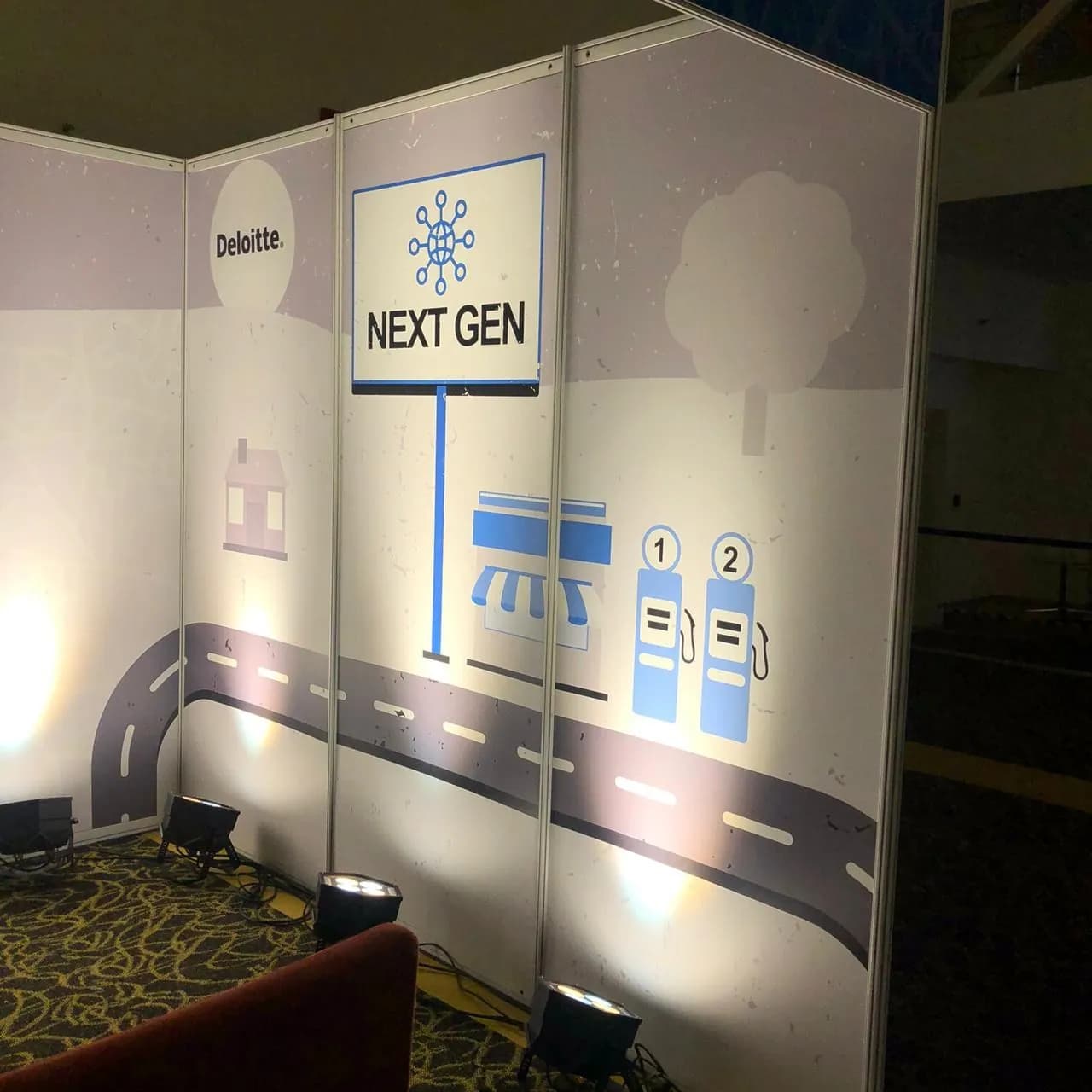Deloitte Next Gen exhibition booth wall with road and fuel-station graphics