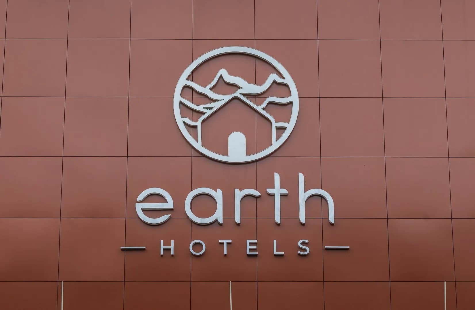 Earth Hotels logo and letters in white metal on a terracotta facade