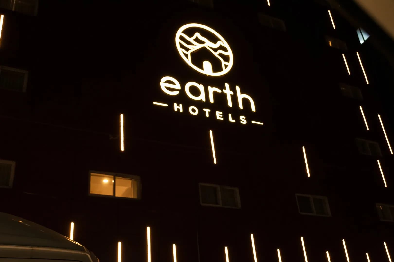 Earth Hotels letters halo-lit at night on a dark facade with vertical light strips