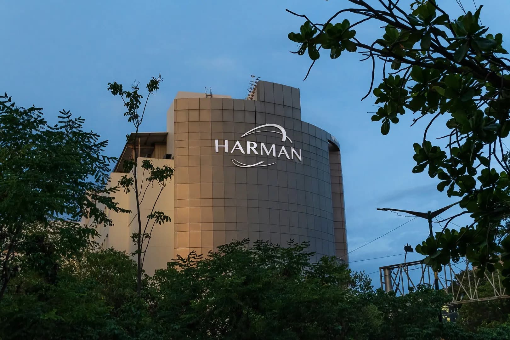 HARMAN sign on a stone-clad office tower at dusk, framed by trees