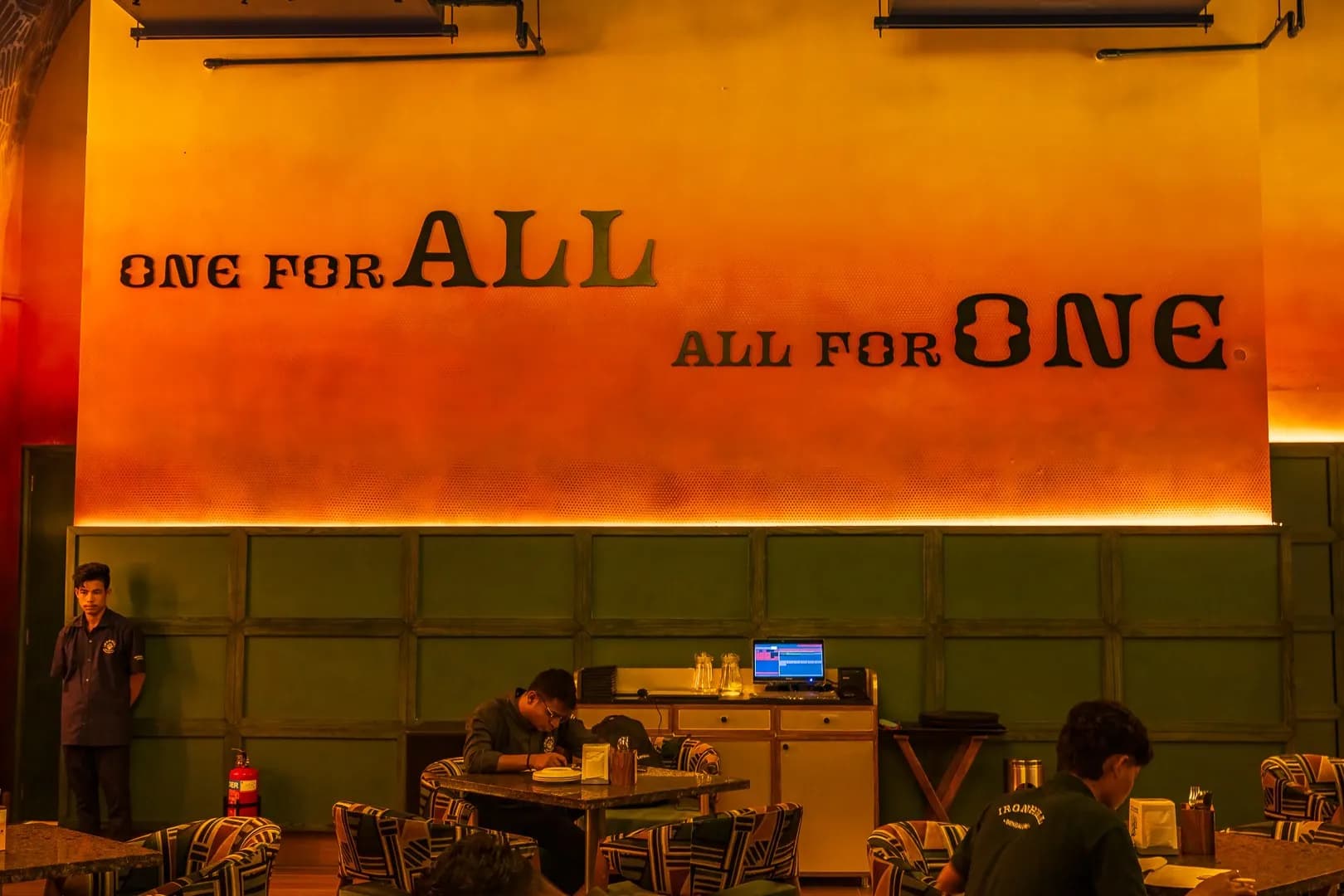 Painted lettering One for all, all for one on an orange wall at Ironhill