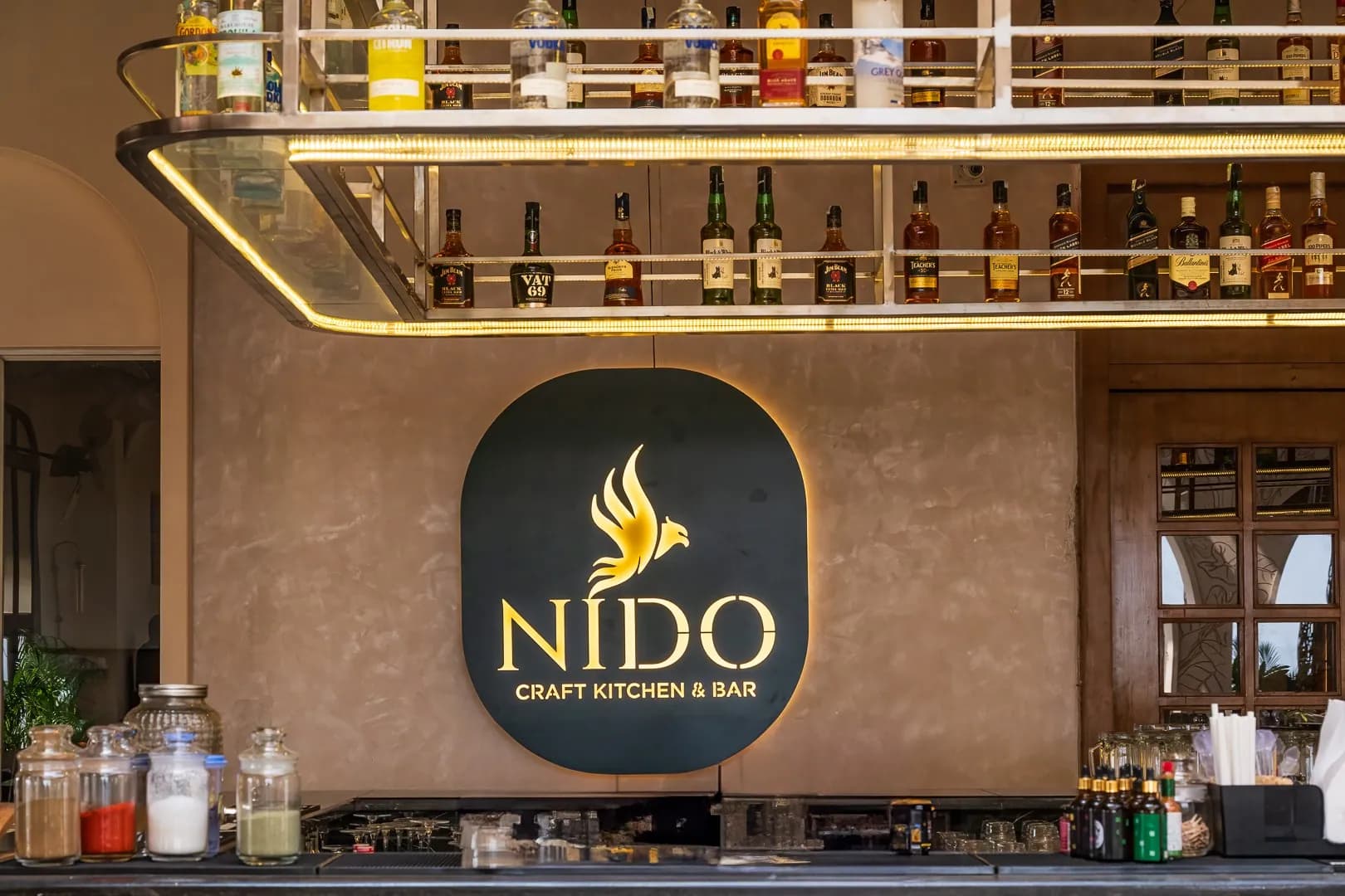 NIDO Craft Kitchen and Bar logo panel, backlit, on the wall behind the bar