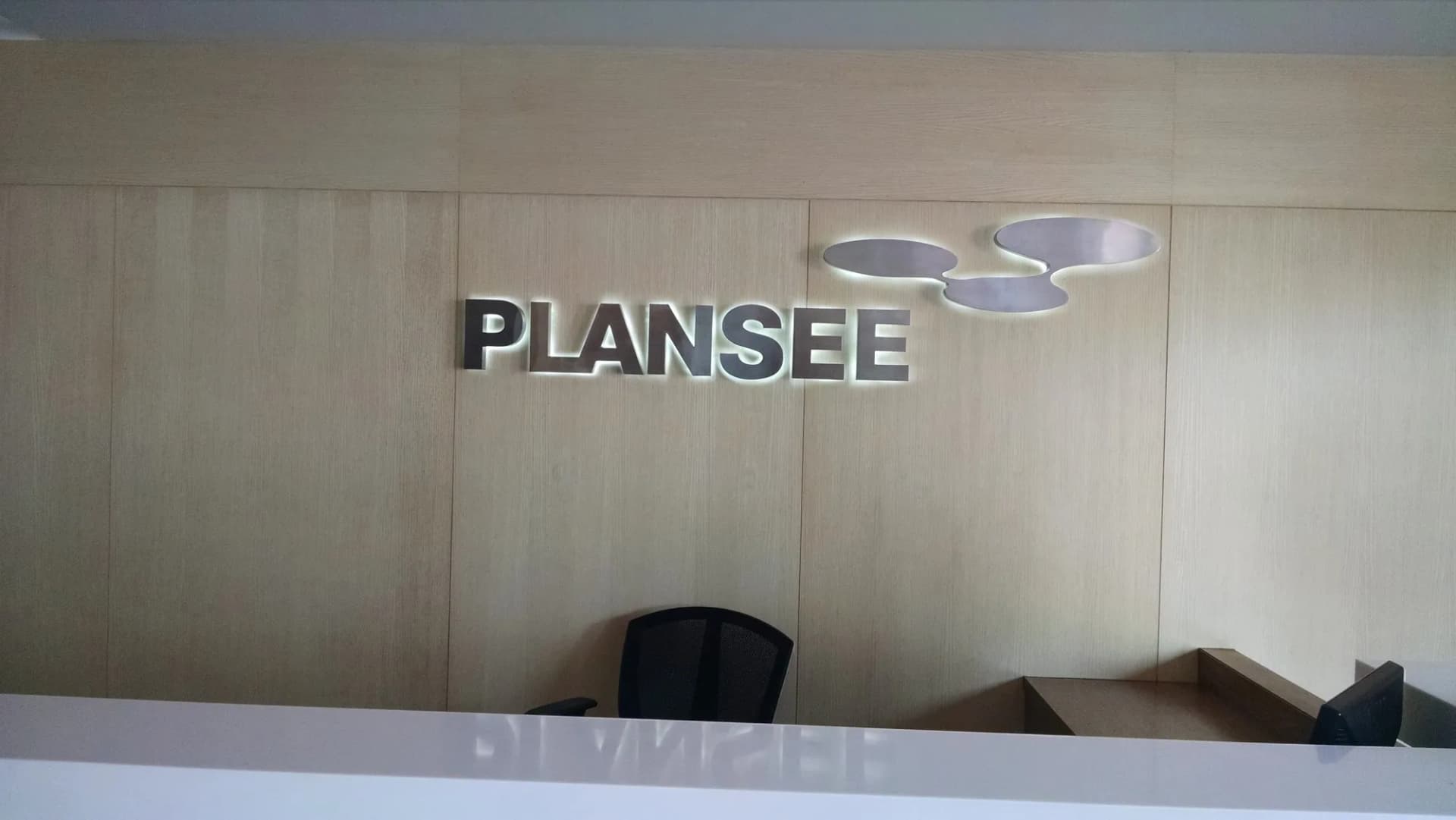Brushed-steel PLANSEE letters and logo on a timber reception wall