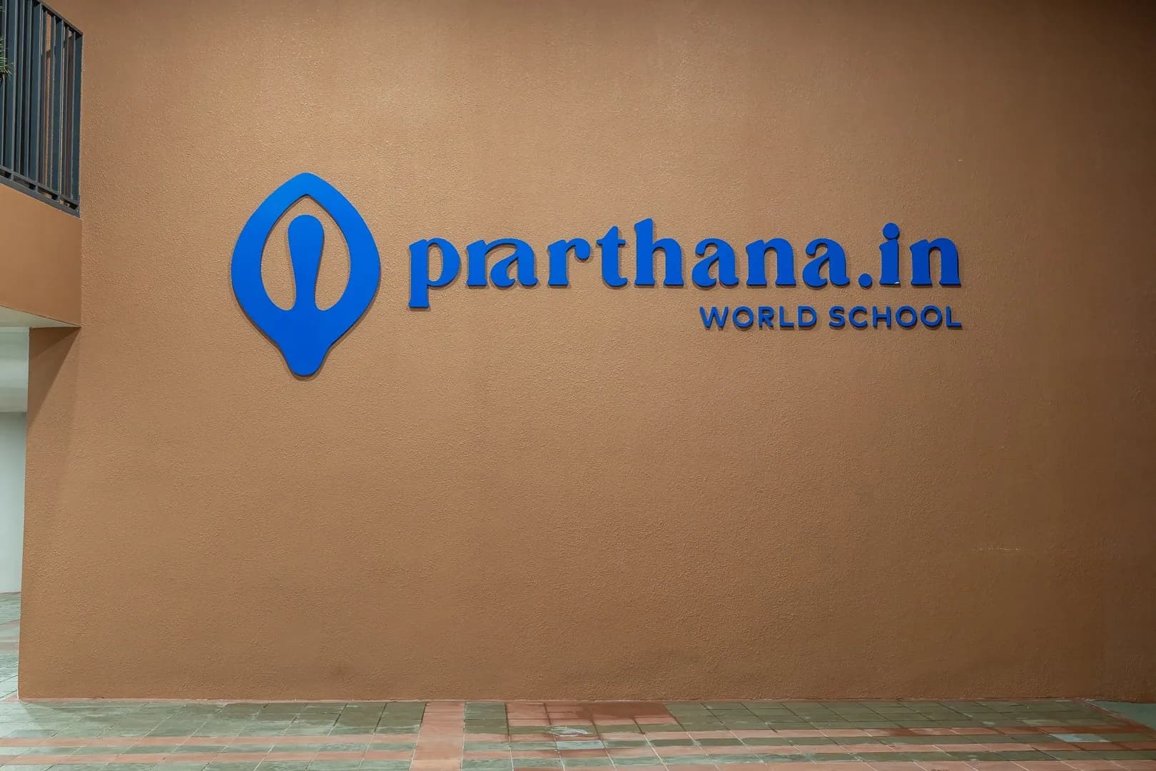 Blue prarthana.in World School letters and logo on a terracotta wall