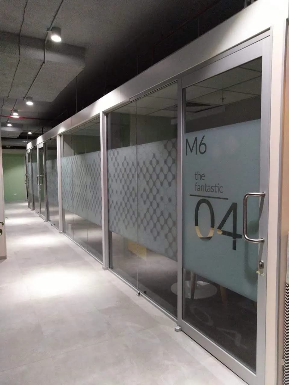 Corridor of glass meeting rooms with patterned frosted film and large room numbers