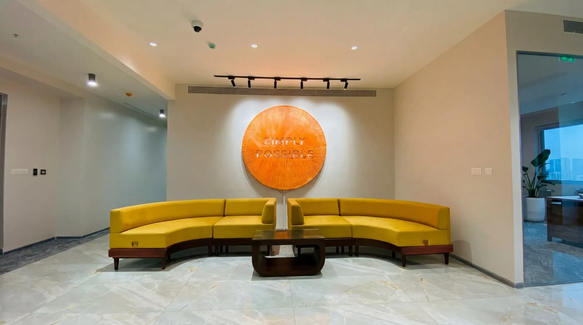 Office lounge with curved mustard sofas under a carved orange disc reading Simply Possible