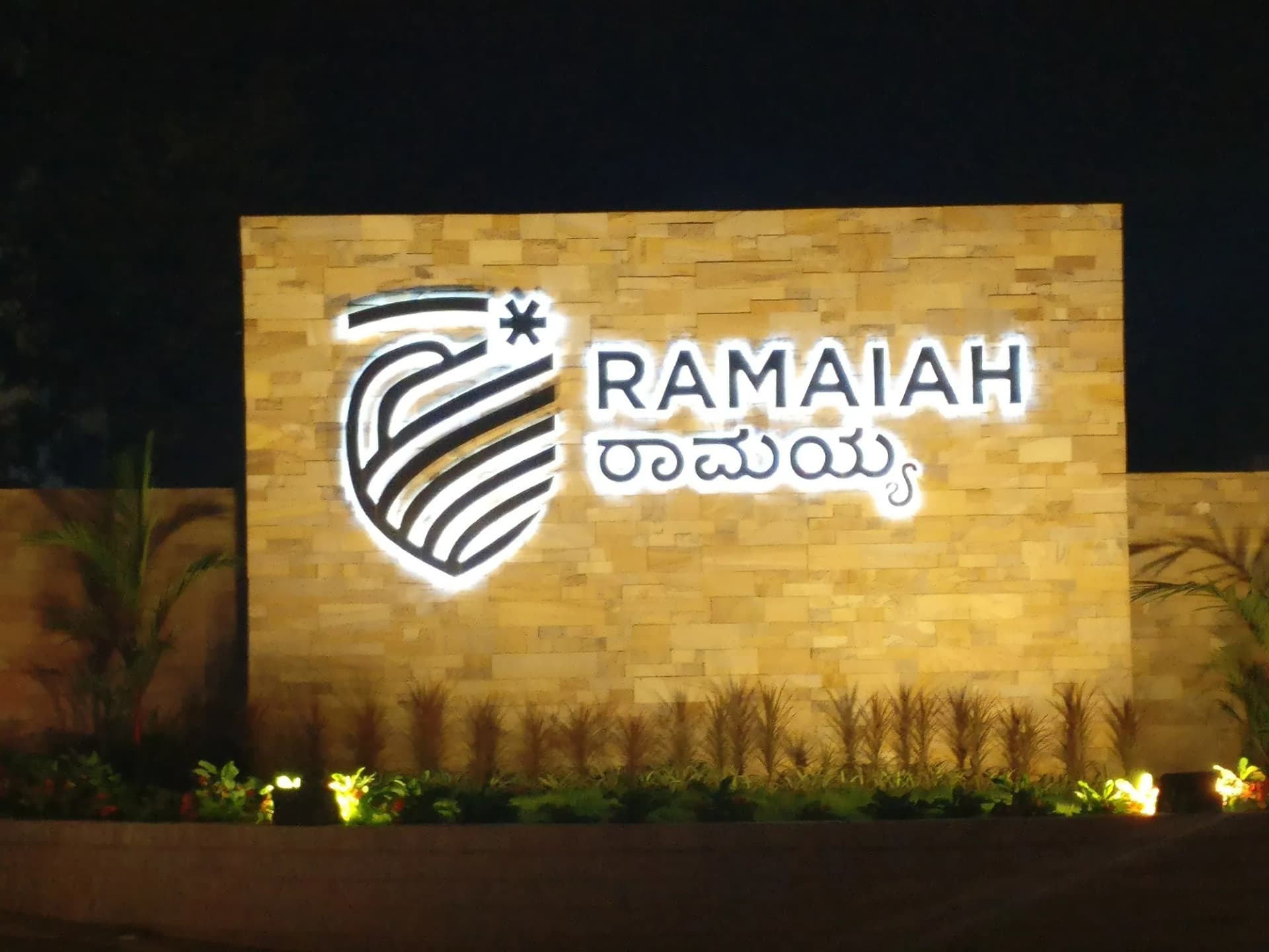 Ramaiah logo and letters lit at night on a stone-clad entrance wall
