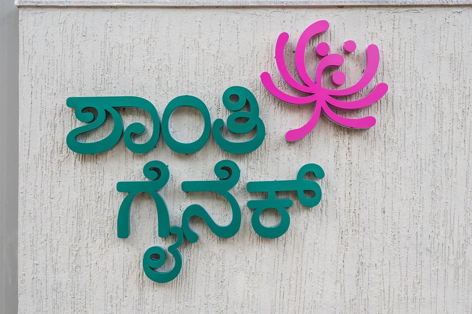 Green Kannada letters and a pink lotus logo for Shanthi Gynec on a textured wall
