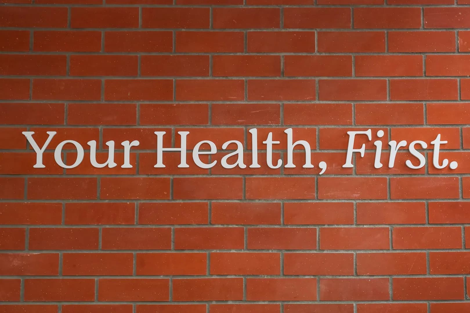White letters reading Your Health, First. on a red brick wall