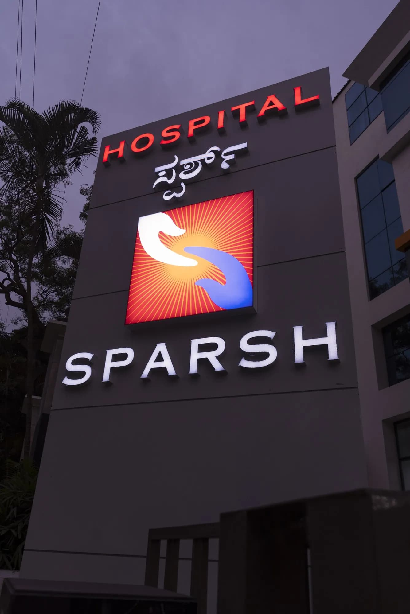Sparsh Hospital tower sign at dusk with red HOSPITAL letters and a lit logo box
