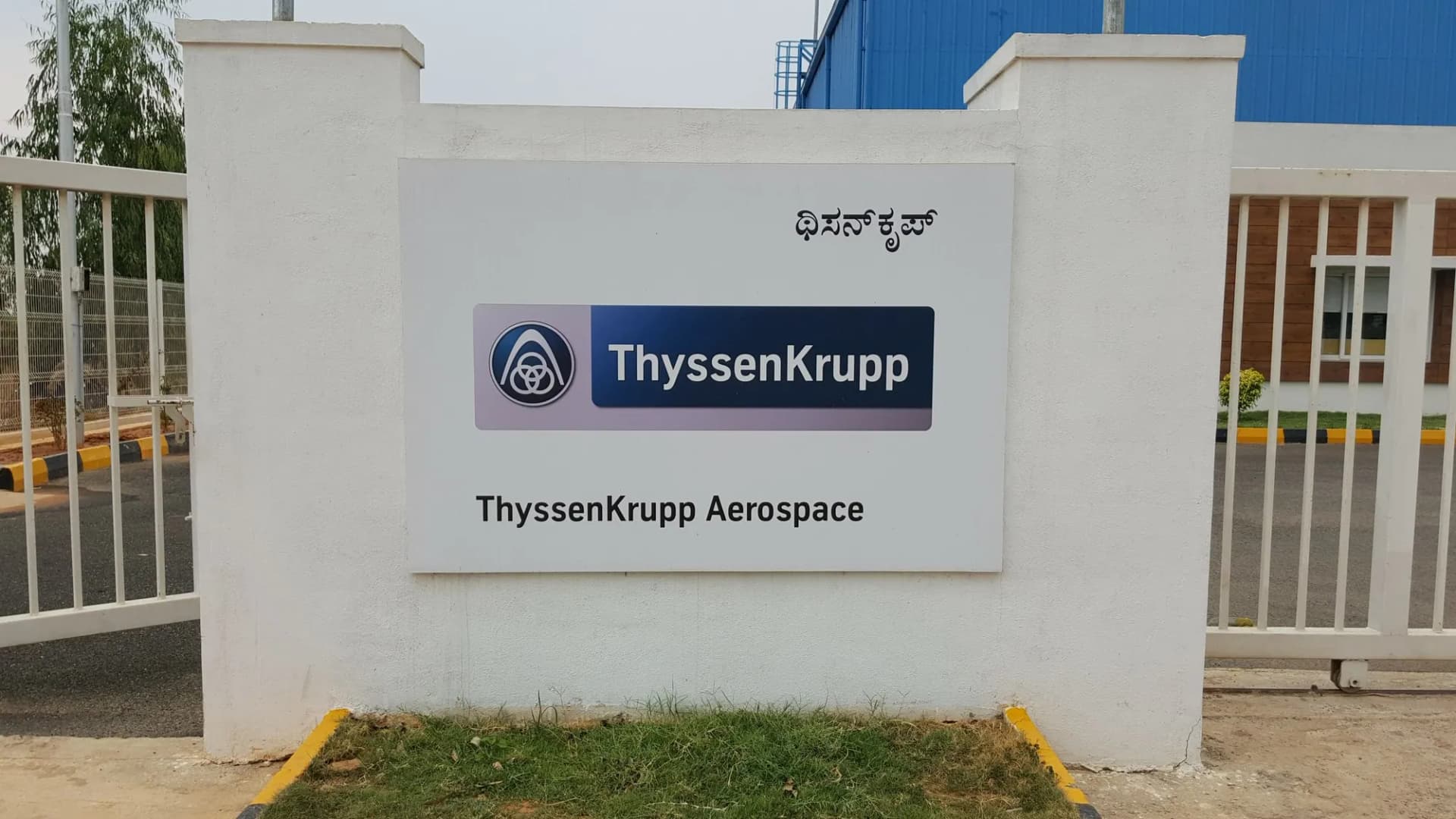 ThyssenKrupp Aerospace sign panel with the name in Kannada on a gate wall