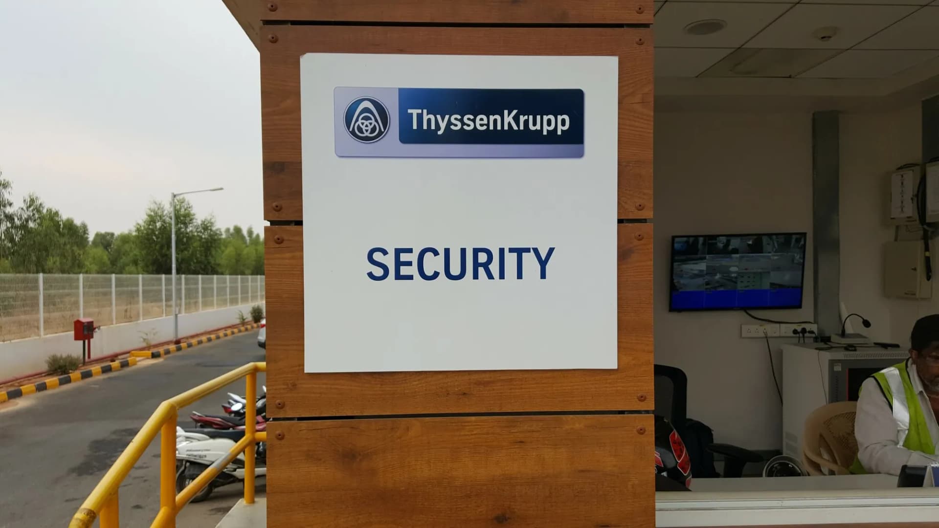 ThyssenKrupp security cabin sign on a timber-clad pillar at a factory gate