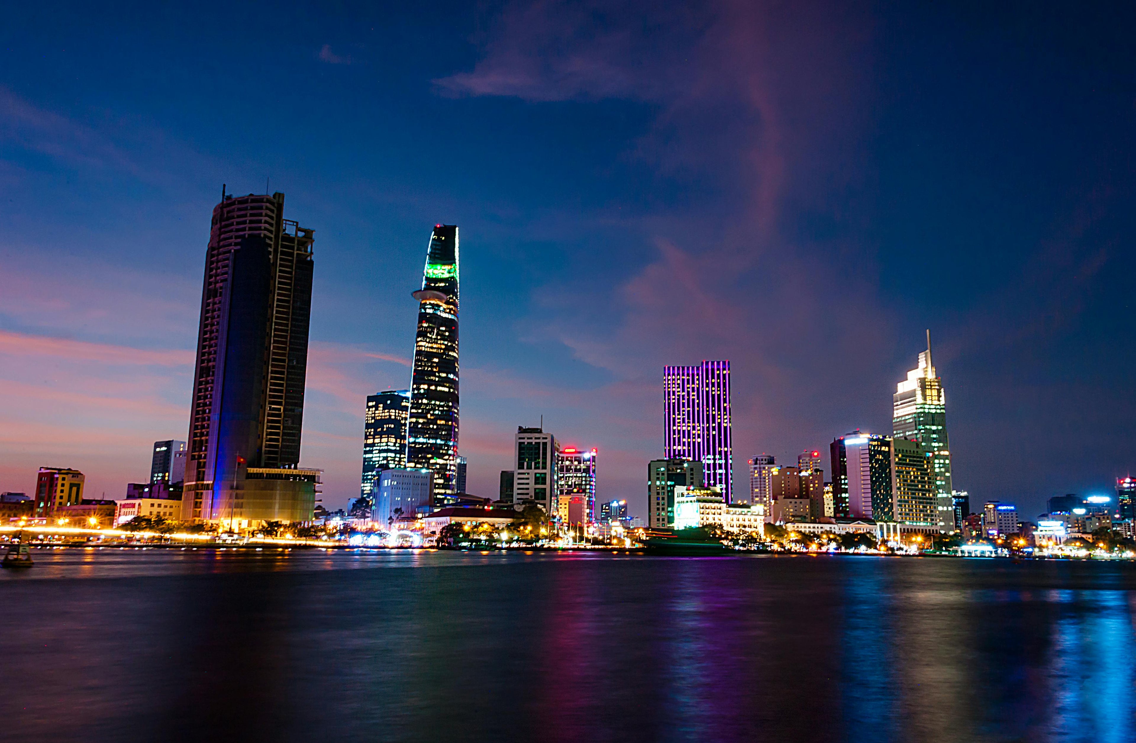 Night cityscape of illuminated skyscrapers reflecting on calm river water under a twilight sky